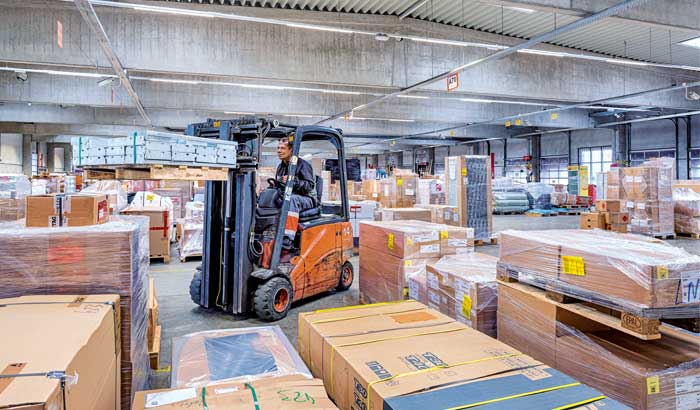 A worker operates a forklift to move palettes in a warehouse
