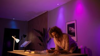 A person is bent over a desk at home, in a room with colorful ambient lighting